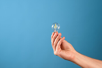 Take a small idea and create something big, new and innovative. A small vintage incandescent lamp in a man's hand, blue background.