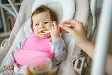 Small caucasian baby reacting on first meal negative emotion child frowns while eating do not like...