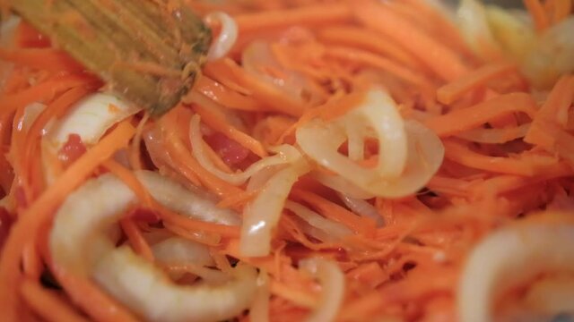 Wooden spoon stirring yam, carrots, tomato, and onion slices in pot