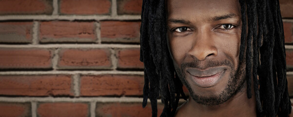 Close-up portrait of a handsome man with dreadlocks standing in front of a brick wall, photo,...