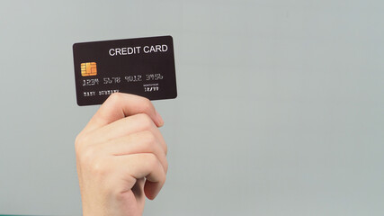 Hand is holding black credit card isolated on grey background.