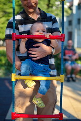 Fototapeta premium Father holding his little baby boy on playground ladder