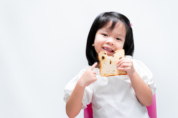 A sweet smiling little girl, a child holding a raisin bread, kid pointing a finger at the bread,...