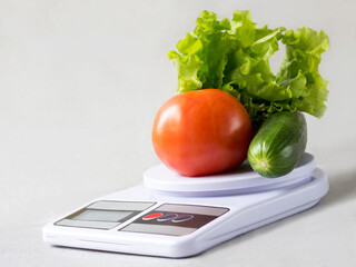 Tomato, cucumber and lettuce leaves on kitchen scales. Healthy nutrition.