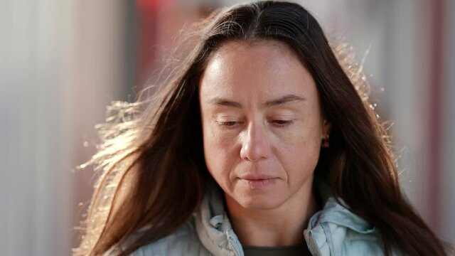 Close-up of the face of an adult woman on the street during the day is sad and looks down. Portrait of a woman without makeup natural beauty
