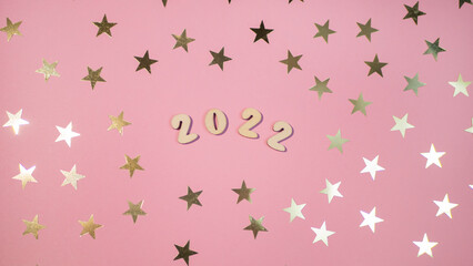Cheerful wooden lettering happy new year 2022 on a soft gently pink background with gold stars. Sparkle confetti holiday concept 