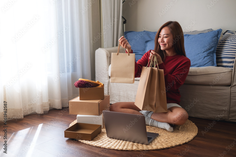 Wall mural a woman using laptop for online shopping , holding shopping bags and opening postal parcel box at ho