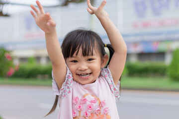 Portrait​ image of​ 3-4 years old​ childhood​ child. Face of smile and laugh Asian​ girl in head shot. Happy​ kid playing​ at the park playground. In summer or spring​ season.