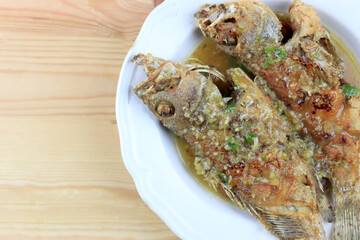 Thai Giant gourami fish and garlics deep fried and sweet spicy sauce in white dish on pine wooden table. Deep fried fish with Sweet chili. Thai food fried fish with spicy sauce. Thai style food.