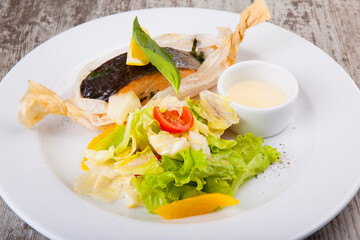 baked trout in paper with salad and white sauce