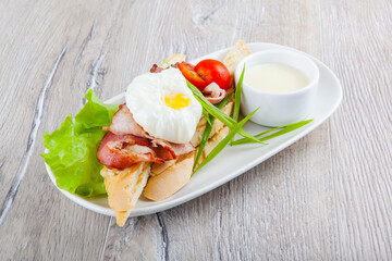 poached egg with bacon cherry tomatoes onion on a baguette and white sauce