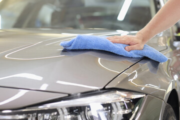 Hood of gray car is wiped with microfiber at car wash