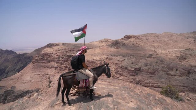 Man on Mule by Jordanian National Flag on Lookout Above Petra Archaeological Site and Canyon, Full Frame, Pan