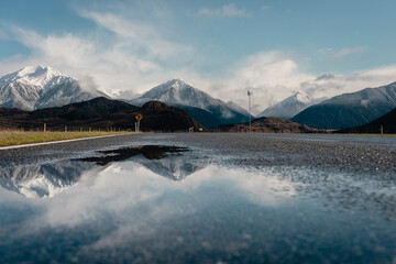 Fototapeta na wymiar Snowy peaks reflected on a puddle from the road. Canterbury, New Zealand