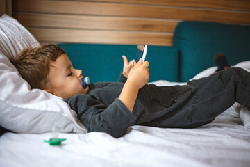 Close up of little boy watching cartoons on the digital tablet at morning with copy space. Close up of adorable kid laying down on the bed by holding a tablet. 