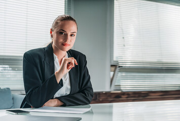 Businesswoman wearing formal suit is touching her chin with pen