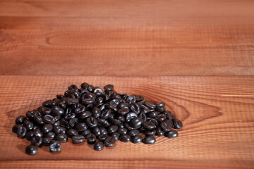 Handful of coffee beans on the background of natural wood texture with text space: making high-quality coffee in the morning, morning drink for energy, vertical image