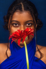 portrait of dark skinned Indian woman from Malaysia against a dark blue background, with flower