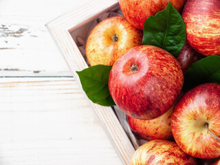 Close up of fresh organic apples and green leaves in wooden box on the white wooden background. Vertical. New Zealand gala variety. Copy space