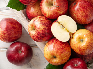 Close up of red and yellow organic apples in wooden box with green leaves on the white wooden background with sliced apple in the top. Top view. Horizontal. New Zealand gala variety.