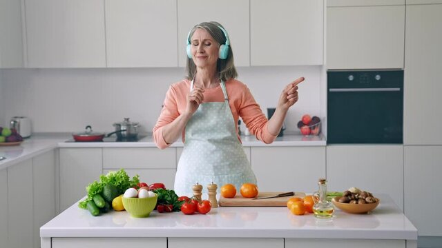 Carefree cheerful nice grandma cook meal listen headphones music motivation