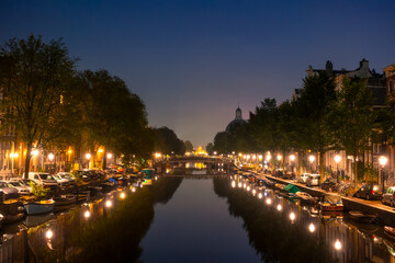 Fototapeta na wymiar Night Canal in Amsterdam With Parked Boats and Cars