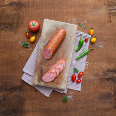 Sausage on wooden cutting board with vegetables, greens and spices. Food background. Top view.