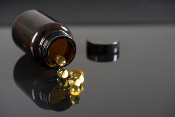 The tablets lie on a mirrored black background, reflect in it. Dark bottle with medicine out of focus.