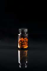 A dark transparent bottle of medicine stands on a black mirrored table.