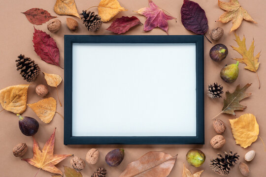 Autumn flat lay with leaves, figs, walnuts and cones on light brown background. Blank picture frame in the center. Mock up, top view, copy space
