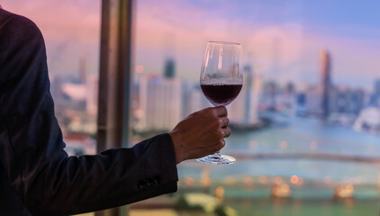 Back view of Man hand with wineglass which he is  Drinking Red Wine From Glass At Winery on the rooftop with city view in the  Restaurant