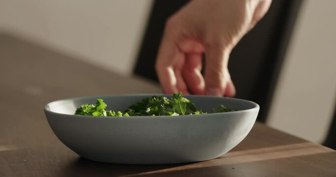 Slow motion put kale in blue bowl on walnut table making salad