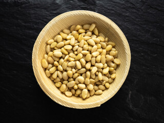 Pine nuts in a bamboo bowl on slate worktop, background. Flat lay, top view.