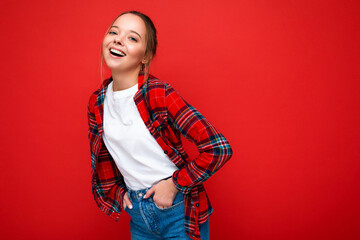 Young beautiful woman in stylish red hipster shirt and casual white t-shirt for mockup. Positive female shows facial emotions. Funny model isolated on red background with free space