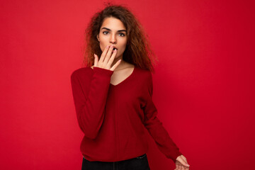 Photo of youngshocked amazed attractive brunette curly woman with sincere emotions wearing casual red sweater isolated on red background with copy space