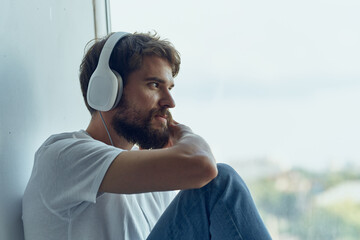 man in white t-shirt sitting on the windowsill in headphones in headphones Lifestyle