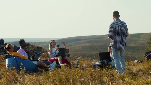 Office people work in the fresh air and communicate. Colleagues are working on laptops, listening to a lecture from a man in hipster clothes and smiling. Coworking concept