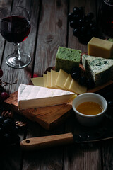 Cheese plate on a dark background. Brie, dor blue, gouda, grapes, nuts, wine