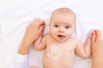 mom's hands hold a baby girl with a smile of cream on her stomach in a crib on a white cotton bed, hygiene and newborn care