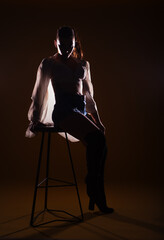 Full-length silhouette portrait on a dark background of a sensational woman posing with a high chair