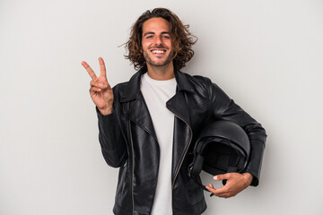 Young biker caucasian man holding a motorbike helmet isolated on gray background showing number two...