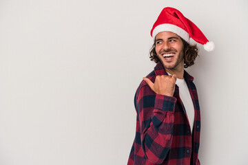 Young caucasian man celebrating Christmas isolated on gray background points with thumb finger away, laughing and carefree.