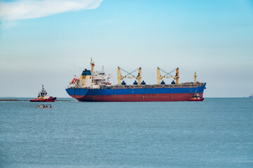 A cargo ship leaving the port with a guide