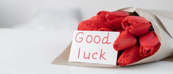 A bouquet of red tulips and a card with the inscription good luck on a white background. Flowers in craft paper. Flower delivery for the holiday.