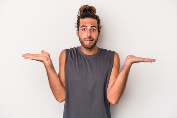 Young caucasian man isolated on gray background confused and doubtful shrugging shoulders to hold a copy space.