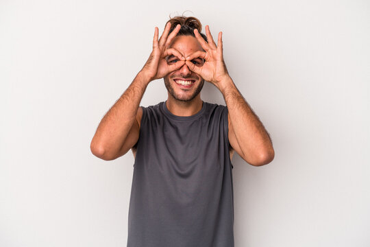 Young caucasian man isolated on gray background showing okay sign over eyes