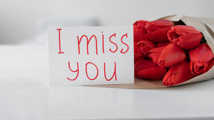 Flowers to a woman. Bouquet of red tulips and greeting card with handwritten inscription I miss you on a white background. Flowers delivery