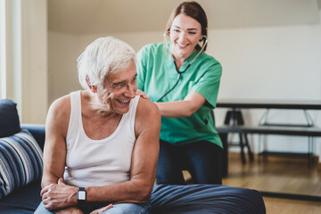 Obraz premium happy female nurse with a stethoscope visiting an elderly man, domestic medical assistant concept, smiling health visitor and a senior male patient, heartache prevention, copy space