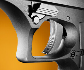 Closeup of a semi automatic handgun trigger with an orange background