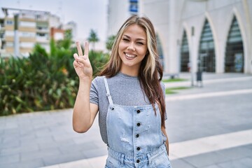 Young caucasian woman outdoors smiling with happy face winking at the camera doing victory sign....